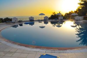 a large swimming pool with a sunset in the background at Holiday Apartments Maria with pool and Panorama View - Agios Gordios Beach in Agios Gordios