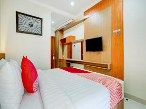 1 dormitorio con 1 cama blanca con almohadas rojas y TV en Super OYO Capital O 90291 Vin Stay Petanu en Pesanggaran