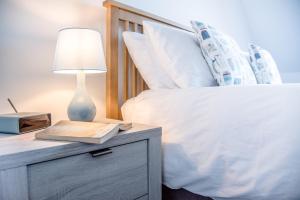 a bed with a nightstand with a lamp and a book at 3 Oaks Court, Thorpeness in Thorpeness
