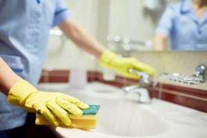 Eine Person in gelben Handschuhen, die einen Schwamm auf einer Spüle schrubbt in der Unterkunft Hotel Royal City in Shiliguri