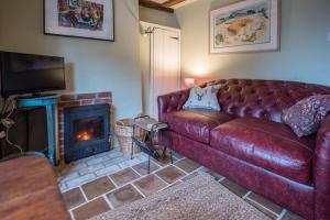 - un salon avec un canapé en cuir et une cheminée dans l'établissement Library Cottage, Marlesford, à Woodbridge