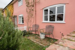 trois chaises assises à l'extérieur d'une maison rose dans l'établissement Library Cottage, Marlesford, à Woodbridge