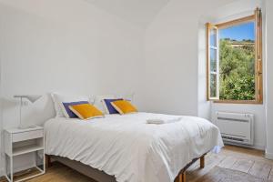 a white bedroom with a bed and a window at Cargèse, appartement de charme surplombant le port in Cargèse