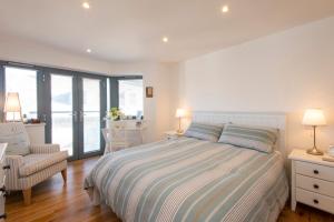 a bedroom with a bed and a chair and windows at Sandpiper Cottages in Newquay