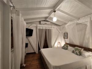 ein Schlafzimmer mit einem weißen Bett mit Vorhängen und einem TV in der Unterkunft Kazalao in Prise dʼEau