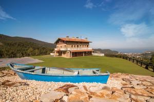 a blue boat sitting on the rocks in front of a house at AGROTURISMO ZUMINTXAZ in Mungia