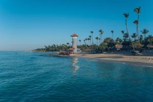 a lighthouse on a beach with palm trees and the ocean at Iberostar Selection Hacienda Dominicus in Bayahibe