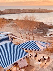 un grupo de personas sentadas bajo sombrillas azules y blancas en una playa en Catalina Beach House by Cassai, en Colonia de Sant Jordi