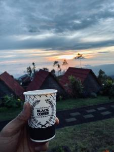 uma mão segurando uma xícara de café com um pôr do sol no fundo em Alengkong Double View em Kintamani