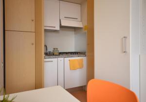 una piccola cucina con armadi bianchi e una sedia arancione di Residenza Casa Mare a Lignano Sabbiadoro