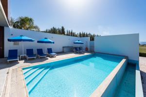 einen Pool mit blauen Stühlen und Sonnenschirmen in der Unterkunft Seafront Villa Sea Gem - Private Beach Area & Infinity Pool in Polis Chrysochous