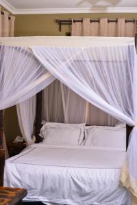 Cama blanca con dosel, sábanas y almohadas blancas en Burka Coffee Lounge, en Arusha
