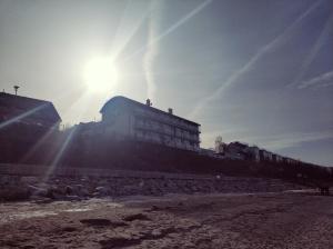 budynek na plaży ze słońcem za nim w obiekcie Na Klifie Cafe Apartament w mieście Ustronie Morskie