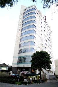 Un edificio alto con un árbol delante. en Shalimar Tower Hotel Lahore, en Lahore
