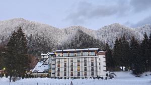 a building in the snow in front of a mountain at Hotel Escalade & SPA in Poiana Brasov