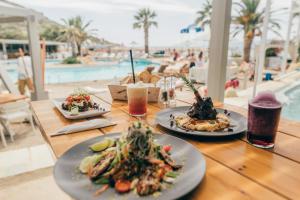three plates of food on a wooden table near a pool at Far Out Village Hotel in Mylopotas