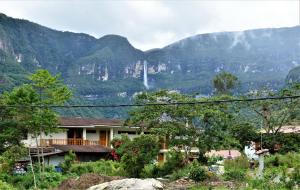 a house in front of a mountain with a waterfall at La Posada de Gocta in Cocachimba