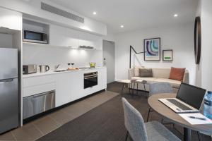 a living room with a kitchen and a table with a laptop at Quest St Kilda Road in Melbourne