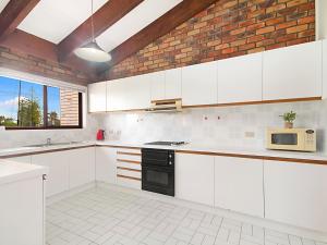 a kitchen with white cabinets and a brick wall at Coral Gardens Unit 2 in Coolangatta