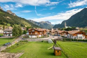 a village in the mountains with a green field at Hotel Arnika in Pozza di Fassa