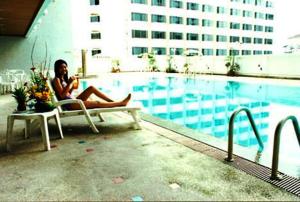 una mujer sentada en una silla junto a una piscina en The Regency Hotel Hatyai, en Hat Yai