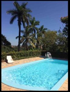uma grande piscina azul com palmeiras ao fundo em Linda Chácara - Águas de São Pedro - Próximo ao Parque Thermas em Águas de São Pedro