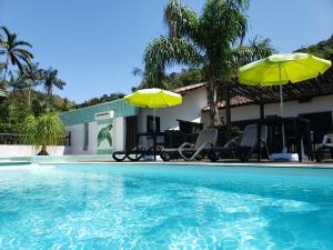 a pool with chairs and umbrellas next to a house at Pousada Tartarugas de Paúba in Pauba