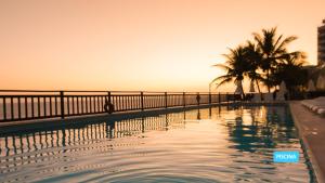 a swimming pool with palm trees and the sunset at Vila Galé Salvador in Salvador