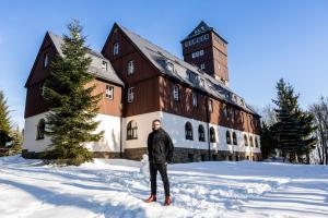 een man die in de sneeuw voor een gebouw staat bij Berghotel Bärenstein in Bärenstein