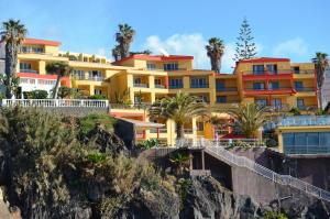 ein gelbes Gebäude auf einem Hügel mit Palmen in der Unterkunft Hotel Cais da Oliveira in Caniço