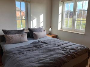 a large bed in a bedroom with two windows at Abendstille, Ferienwohnung für maximal 4 Erwachsene und 2 Kinder in DE FEERJENHUSEN am Haubarg von Vollerwiek in Vollerwiek