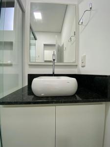 uma casa de banho com um lavatório branco e um espelho. em MaxLoft - Apto novo Smart Tv, lavanderia em Joinville