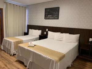 a hotel room with two beds with white sheets at Splendore Hotel in Conceição do Mato Dentro