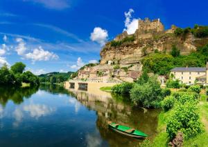 a boat on a river with a castle on a hill at La Petite Maison in Beynac-et-Cazenac