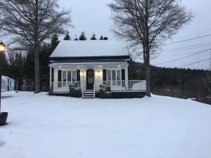 a small white house with snow on the roof at Gîte de la colline in Baie-Sainte-Catherine