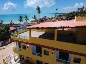un bâtiment jaune avec un toit rouge à côté de l'océan dans l'établissement Flats Parada Obrigatoria, à Maragogi