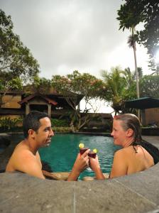 a man and a woman sitting next to a swimming pool at De Munut Balinese Resort in Ubud