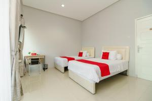 RedDoorz @ Jalan Demang Lebar Raya Palembang في باليمبانغ: سريرين في غرفة نوم بيضاء مع ملاءات حمراء وبيضاء