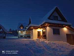 a house covered in snow at night with lights at Noclegi domek in Kościelisko