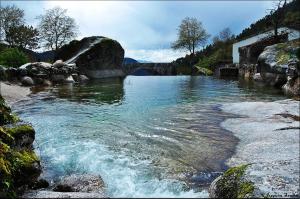a river with a bridge and some rocks and water at Casa da Fonte Sagrada in Loriga