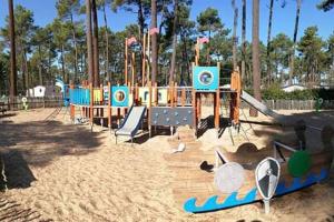 a playground with a slide and surfboards in the sand at Mobil home 6/8 pers Les Dunes de Contis in Saint-Julien-en-Born