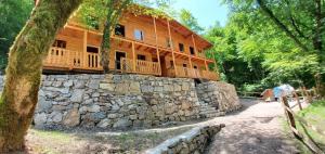 a large wooden house with a stone wall at Park Blini Shala River in Mollʼ e Shoshit