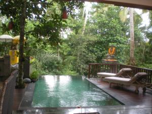 a pool in the middle of a yard with chairs and trees at Harum Sari Ubud Private Villa in Ubud