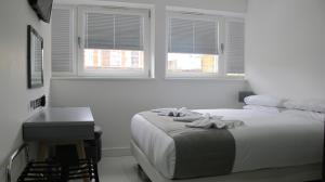 a white bedroom with a bed and a table and windows at BLOOMSBURY APARTMENTS in London