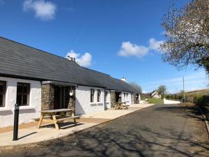 a white building with a bench next to a street at Tavnaghoney Cottages in Cushendall