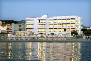 a large white building with tables and chairs next to the water at Hotel Sabbia D'oro in San Vincenzo
