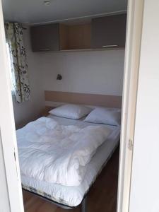 Cama en habitación pequeña con sábanas y almohadas blancas en Luxueuze stacaravan in Bredene met eigen terras en tuintje (425) en Bredene