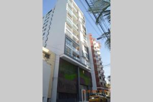 a tall white building on a street with a palm tree at Apartasuite exclusivo VIP El Rodadero Santa Marta in Rodadero