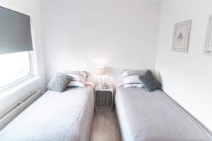 two twin beds in a white room with a window at Bungalow Sunny, lekker uitwaaien op het strand! in Callantsoog