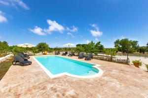 a swimming pool with chairs and umbrellas on a patio at Villa Martina by BarbarHouse in Carovigno